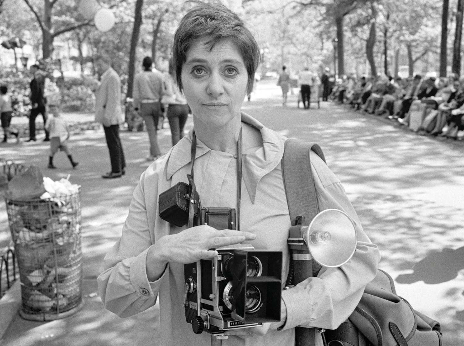 Diane Arbus standing in a park holding cameras