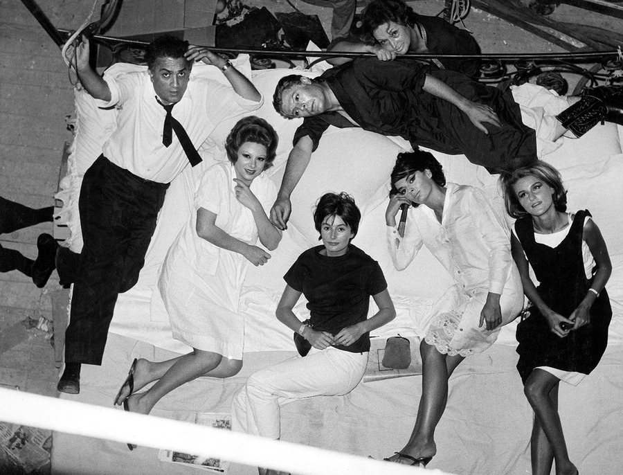 Fellini and his cast all stare at a camera above a bed they are all lying in on the set of 8 1/2